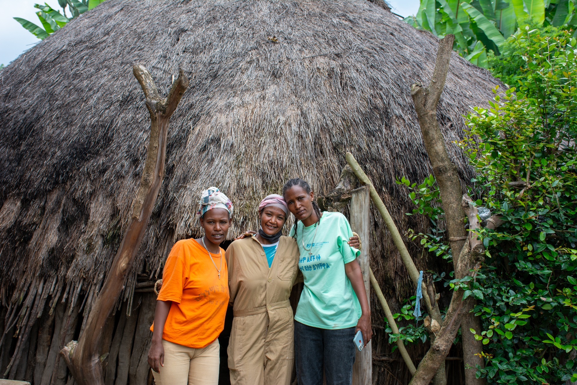 Trois jeunes femmes se tiennent bras dessus bras dessous devant leur entreprise.