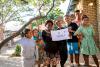 Une famille se tient ensemble sous un arbre et brandit un papier en riant.