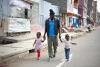 Un père marche dans la rue en tenant ses deux enfants par la main.